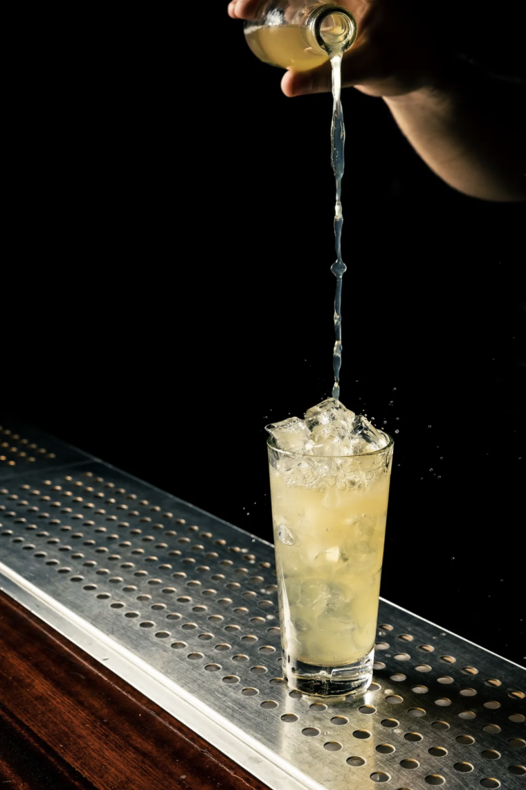 House-made soda being poured into a tall glass over ice
